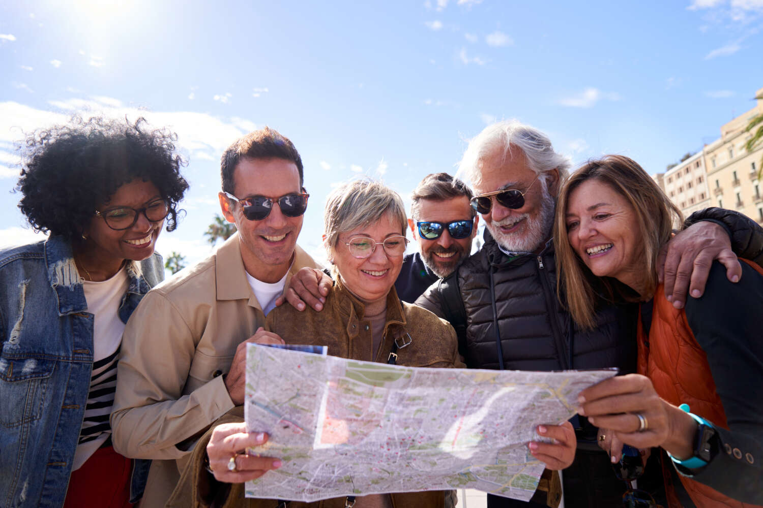 Group of diverse mature travelers smiling and looking at a map during a private guided tour on the charming streets of a historic city in Spain.