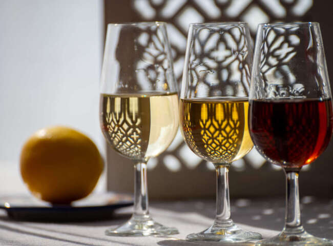 Glasses with cold dry fino and sweet cream sherry fortified wine in summer sunlights, andalusian style interior on background