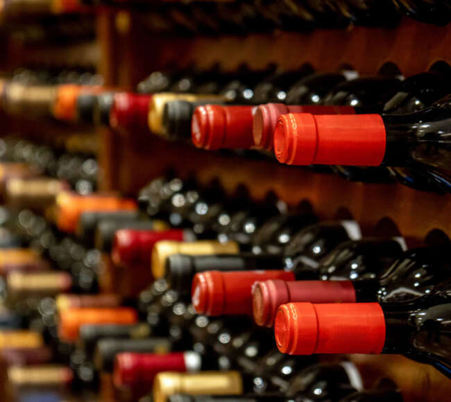 Bottles of black red wine lined up and stacked on wooden wine rack shelves from a private collection of a wine cellar in Spain.
