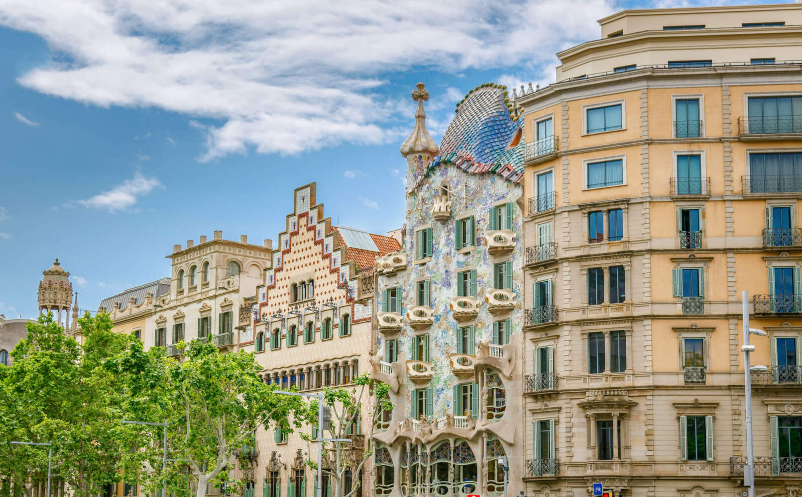 View of Casa Batlló in Barcelona, Spain, showcasing its iconic Modernisme architecture with a colorful mosaic façade, flowing organic lines, sculpted balconies resembling masks, and a wavy roof inspired by natural forms.