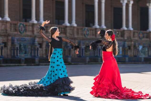 Two women in flamenco colorful costumes dancing outdoors.