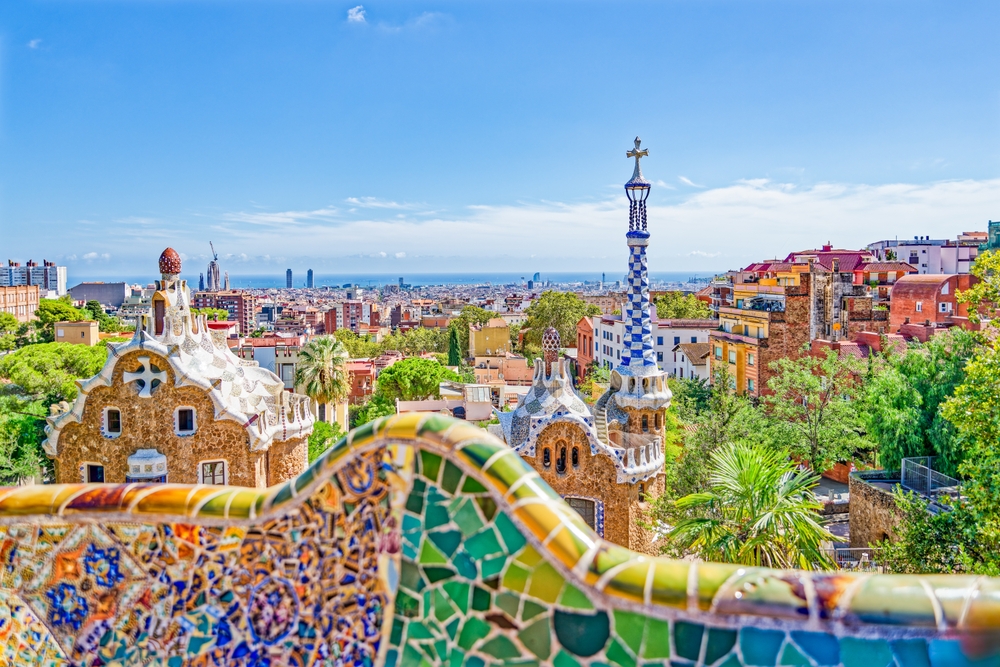 Panoramic view of Park Güell in Barcelona, Spain, showcasing its colorful mosaic benches, whimsical Gaudí-designed architecture, and sweeping city views under a bright blue sky.