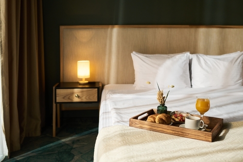 Cozy bed and breakfast in Porto showcased with a breakfast tray filled with coffee, juice, pastries, and fruit, on the bed next to a lamp providing ambient lighting.