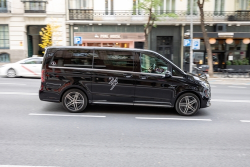 Black minivan transporting passengers with a professional chauffeur service through an urban area in Madrid, Spain.